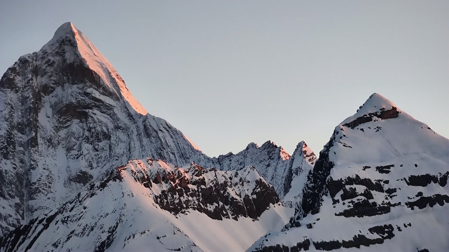 Les premiers rayons du soleil teintent de rose la pyramide sommitale d'un pic du Siguniang au-dessus des crêtes enneigées à l'aube.