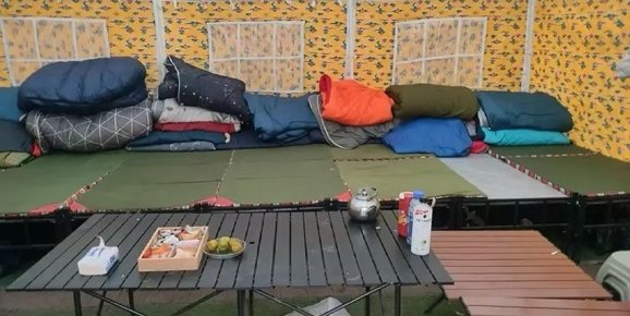 Intérieur d'une tente du camp de base : sacs de couchage et tapis installés sur une plateforme, avec une table basse devant.