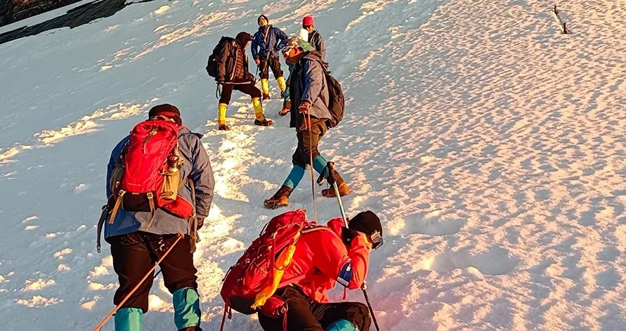 Des grimpeurs avec des sacs à dos rouges montent sur un champ de neige dans la lumière dorée du petit matin, au Siguniang.