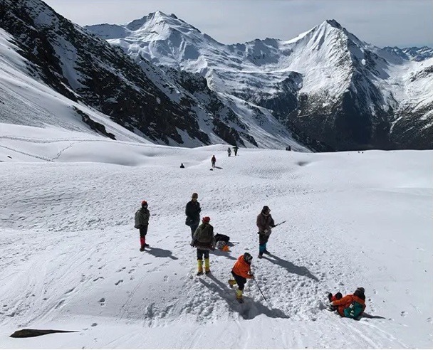 Des grimpeurs traversent un vaste champ de neige sous les sommets du Siguniang.
