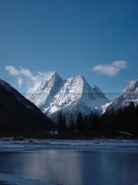 Les sommets enneigés du Siguniang se reflètent dans un lac calme, avec une forêt de pins sombres au premier plan.