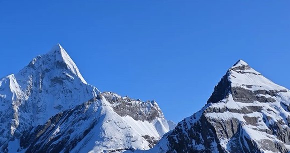 Deux pics acérés et enneigés du massif du Siguniang sur un ciel d'un bleu profond.