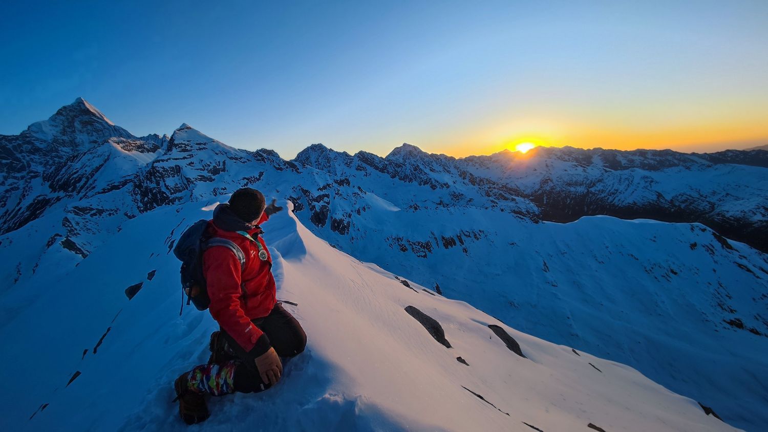 Un grimpeur sur une crête enneigée montre du doigt le soleil qui se lève sur les montagnes près du Siguniang.